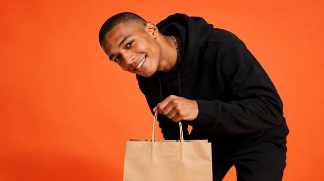 Smiling RunTango rider holding a delivery bag against an orange backdrop